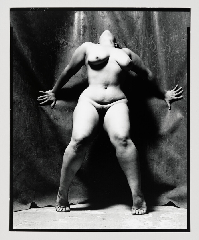 Naked person standing with legs apart and hands pressed against a backdrop, head tilted back.