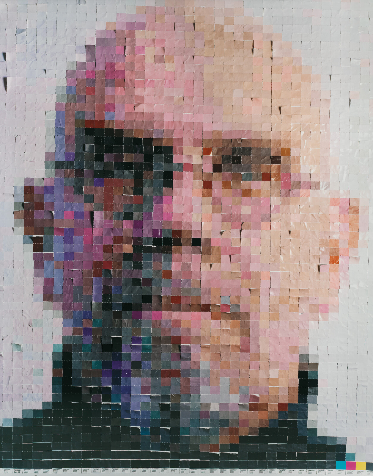 A pixelated portrait composed of numerous square paper notes in various shades of pink, purple, black, and white, creating a mosaic effect. The image resembles a face when viewed from a distance. The bottom of the artwork features a color reference guide.