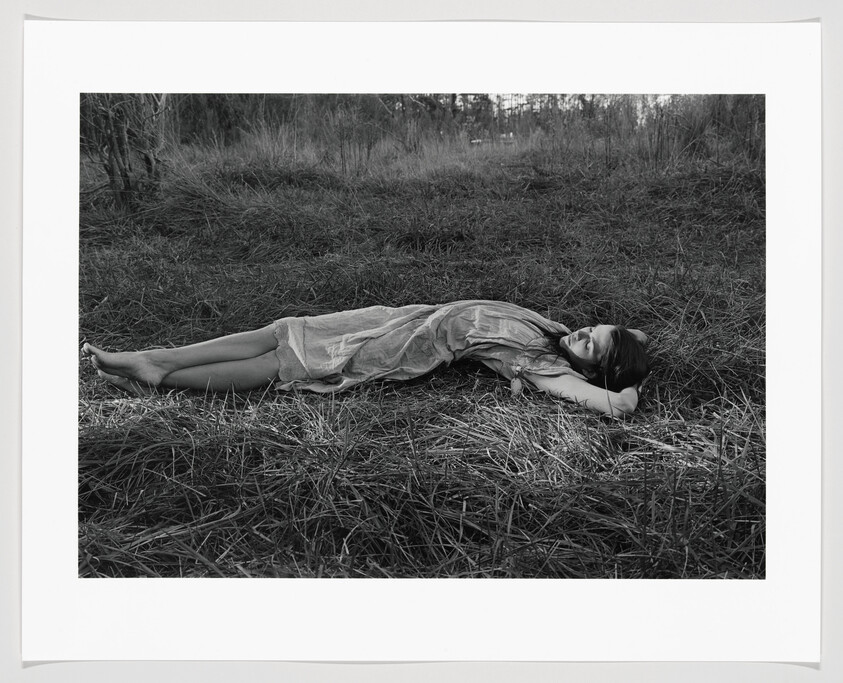 A woman lying on her back in tall grass with her hands behind her head.