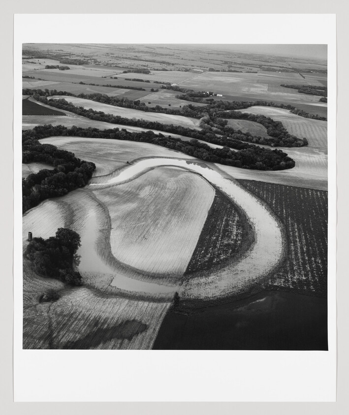 Aerial view of a winding river meandering through flooded farmland and tree-lined riverbanks.