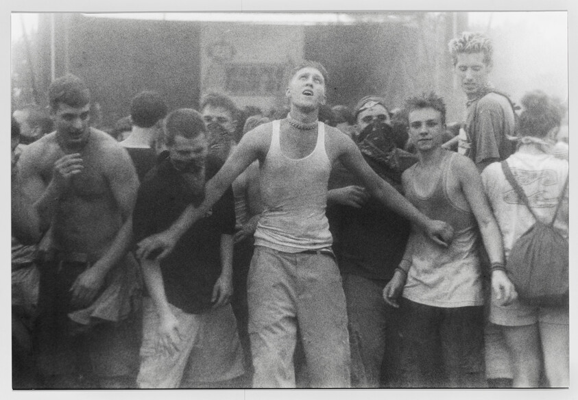 Young people crowded at a concert, central man with arms outstretched and eyes closed.