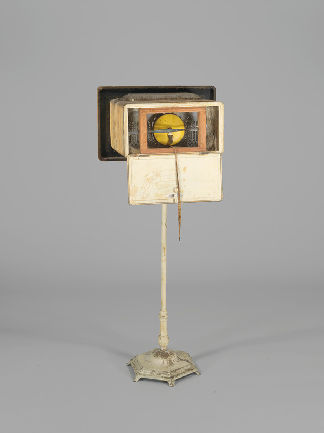 A vintage wooden birdcage-like lantern on a tall painted metal stand with a yellow disk inside.