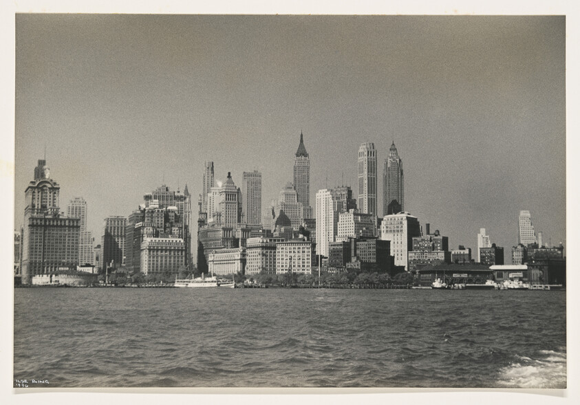 Manhattan skyline with tall buildings rising behind the waterfront and boats on the river.
