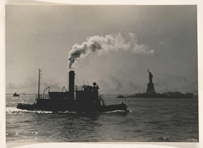 A tugboat belching smoke moves across the water with the Statue of Liberty in the background.
