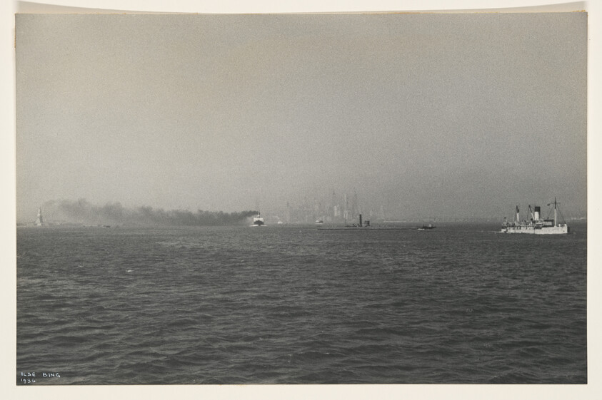 Several ships cross a foggy harbor leaving smoke trails with a distant city skyline visible.