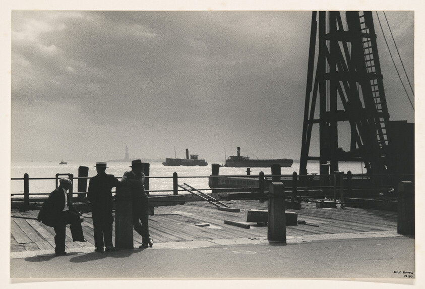 Four men stand on a wooden pier watching steamships pass on a cloudy day.