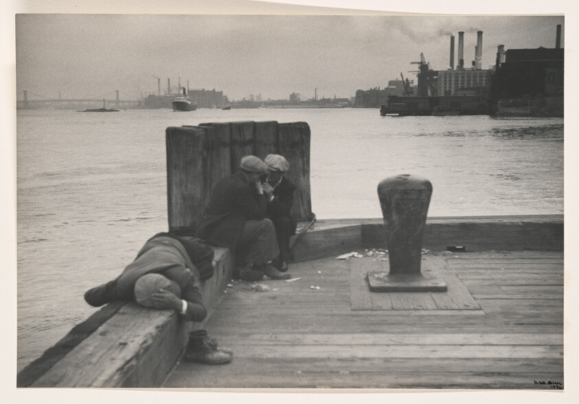 Three dockworkers by the water, two whispering together while a third lies resting on the pier.