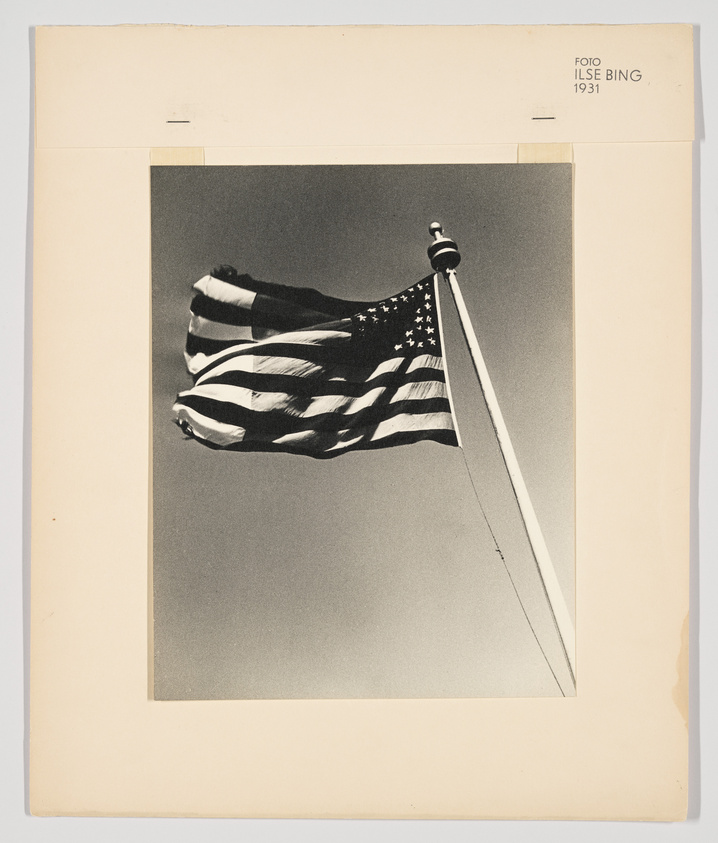 A black and white photo of the U.S. flag atop a pole and flapping in the wind.