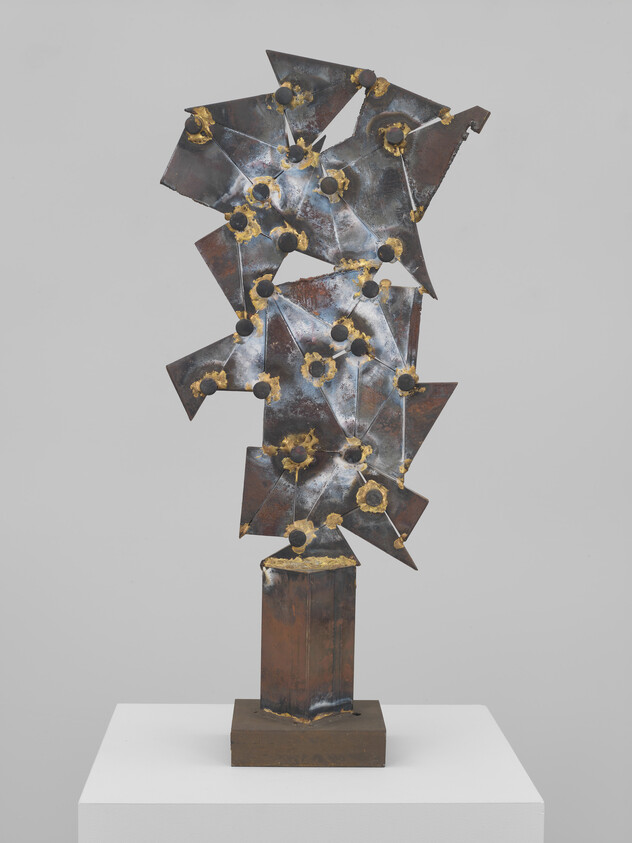 Abstract welded metal sculpture with jagged star-like plates and gold-colored welds on a pedestal.
