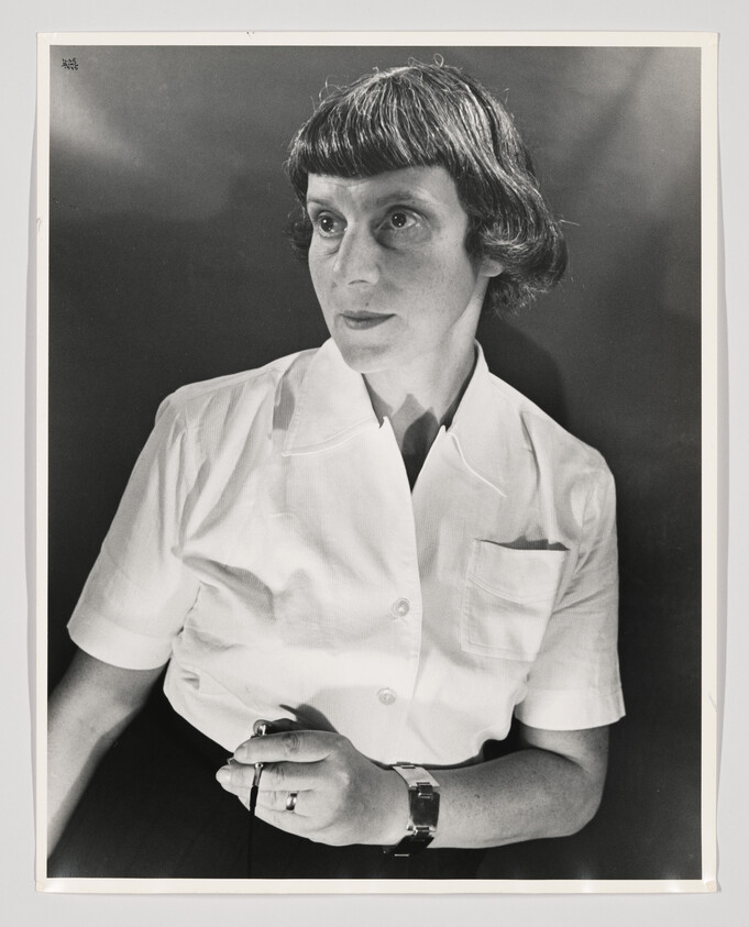 Woman in a white short-sleeve shirt holding a small object and looking off to the side.