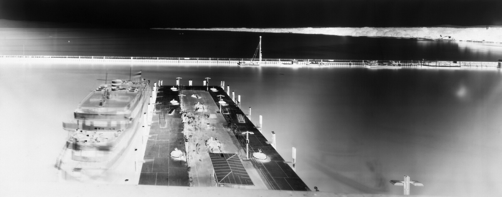 A large ship moored at a quiet pier with a long breakwater in the distance.