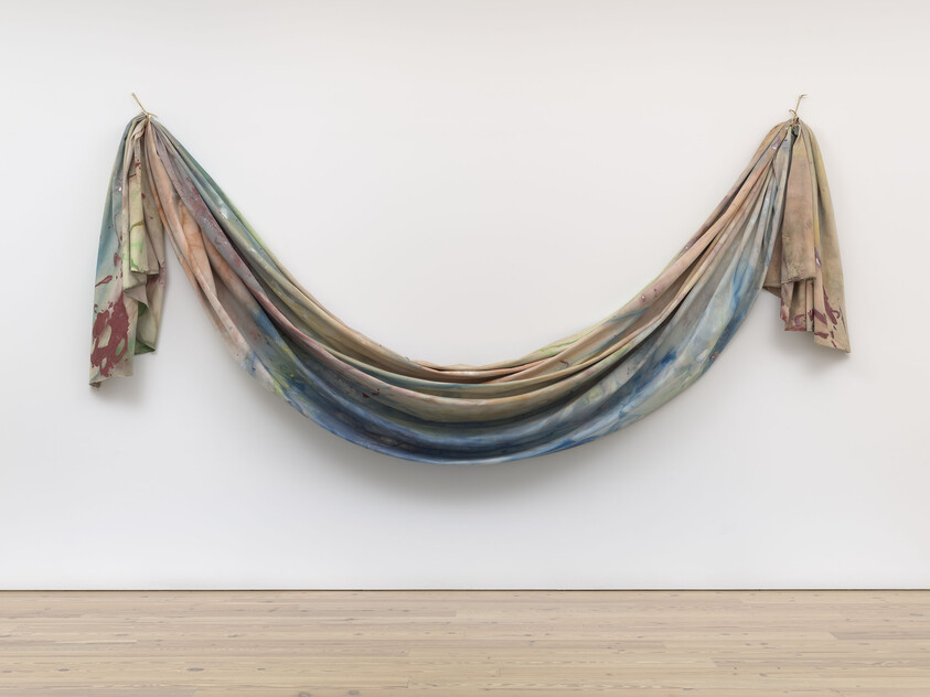 A large, multicolored fabric is draped in a loose curve and hung from two points on a white wall.