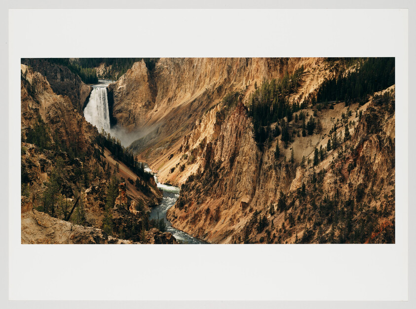 A majestic waterfall cascades down a steep, rocky canyon surrounded by pine trees, with mist rising from where the water meets the river below, which snakes away into the distance.