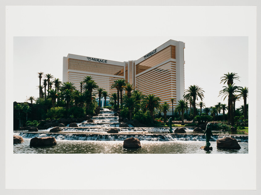 A photograph of The Mirage Hotel in Las Vegas, showcasing its iconic golden windows, with a foreground of palm trees and a multi-tiered water feature.