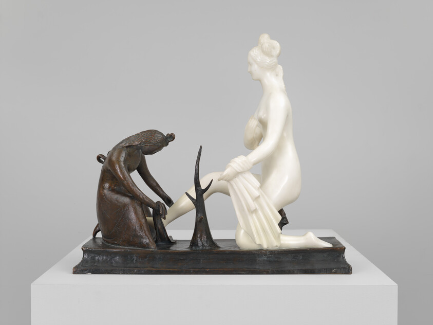 Bronze attendant helps a pale kneeling woman remove her sandal while she lifts a draped cloth.