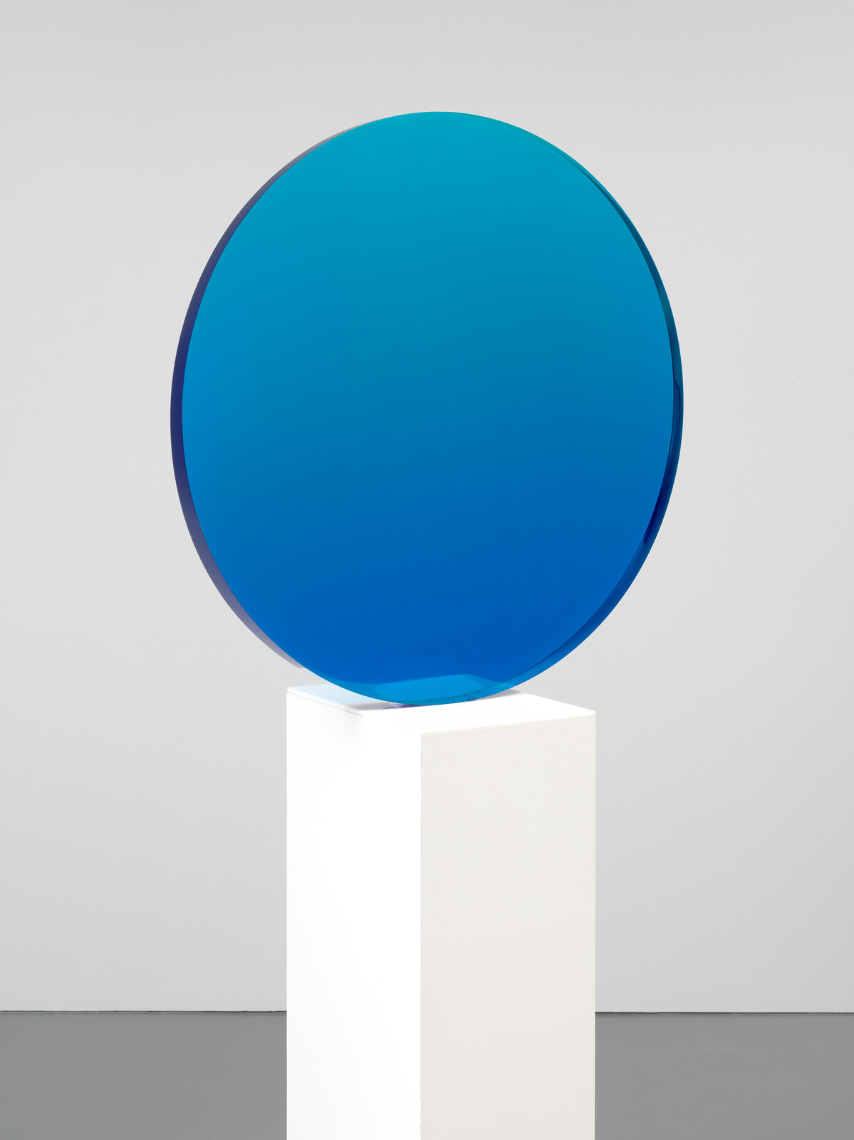 A large circular blue glass disc sits on a white pedestal.