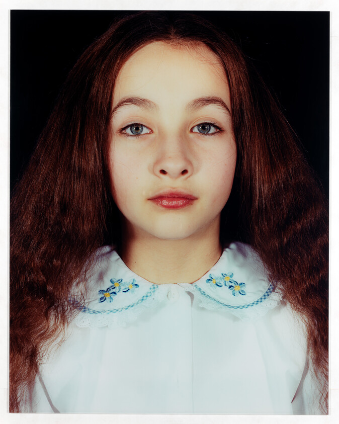 Young girl with long brown hair and embroidered white collar looking directly at the camera.