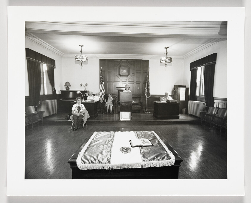 Children seated in a courtroom mock trial while an open book lies on a draped table.