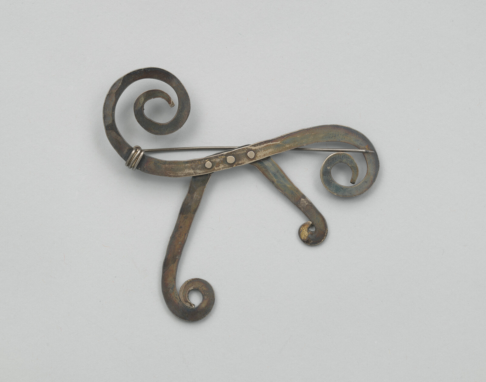 Antique metal brooch with three curled scrolls and a straight fastening pin across the back.