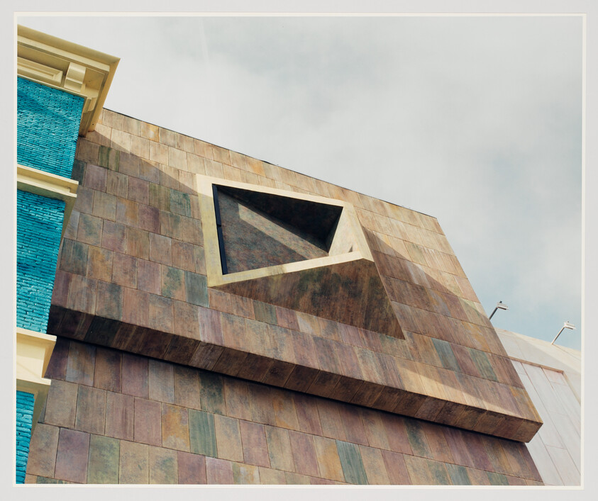 Modern building facade with a geometric window cutout against a cloudy sky.