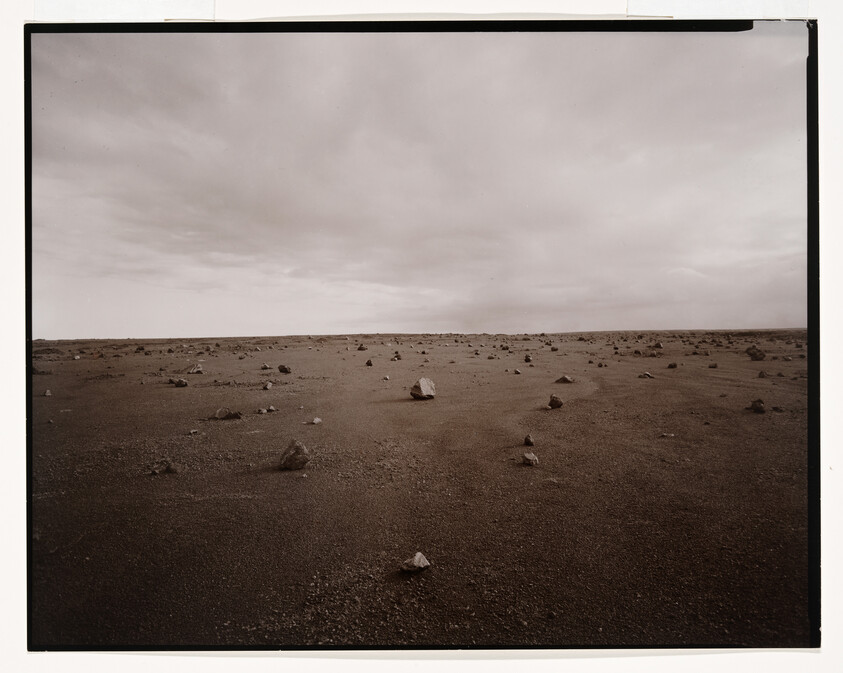 Barren flat plain scattered with small rocks under a wide, cloudy sky.