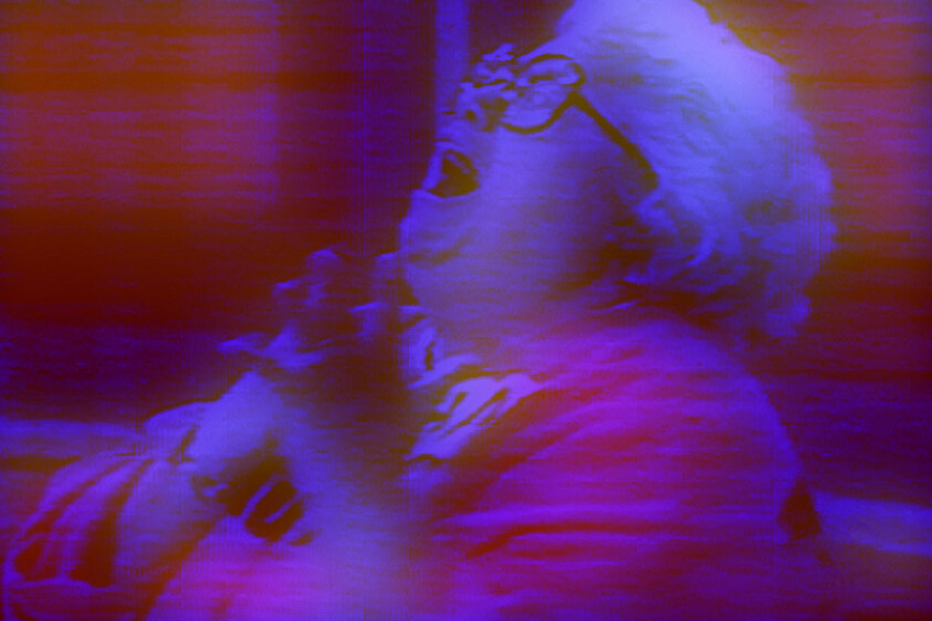 Elderly person with glasses looking upward and clutching chest with shocked expression.