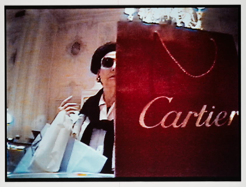 A garnet red Cartier bag sits in front of a white woman as her right arm carry's shopping bags