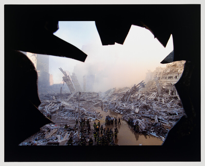 View through a broken window of a devastated urban area with collapsed buildings, debris scattered all around, and emergency responders gathered in groups amidst the ruins. Smoke and dust fill the air, creating a hazy atmosphere.