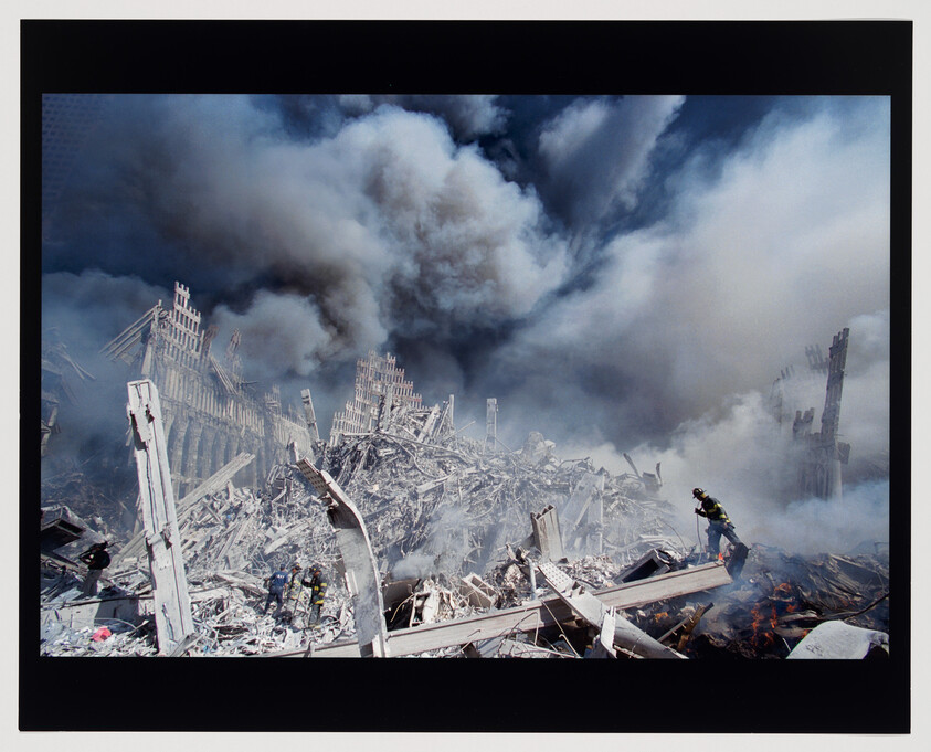 A firefighter searches through smoky debris amid collapsed steel towers and billowing clouds of dust.