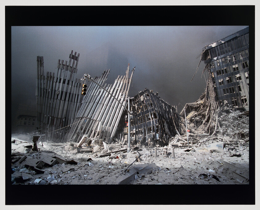 Collapsed steel-framed buildings and debris fill a dusty street beneath a leaning traffic light.