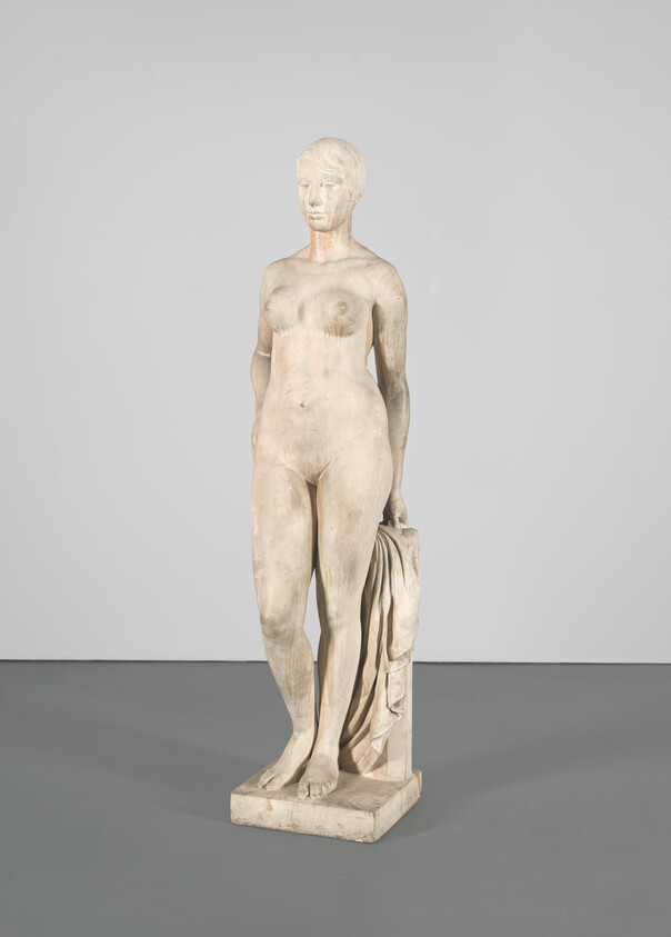 Nude marble statue of a standing woman holding a draped cloth beside her.