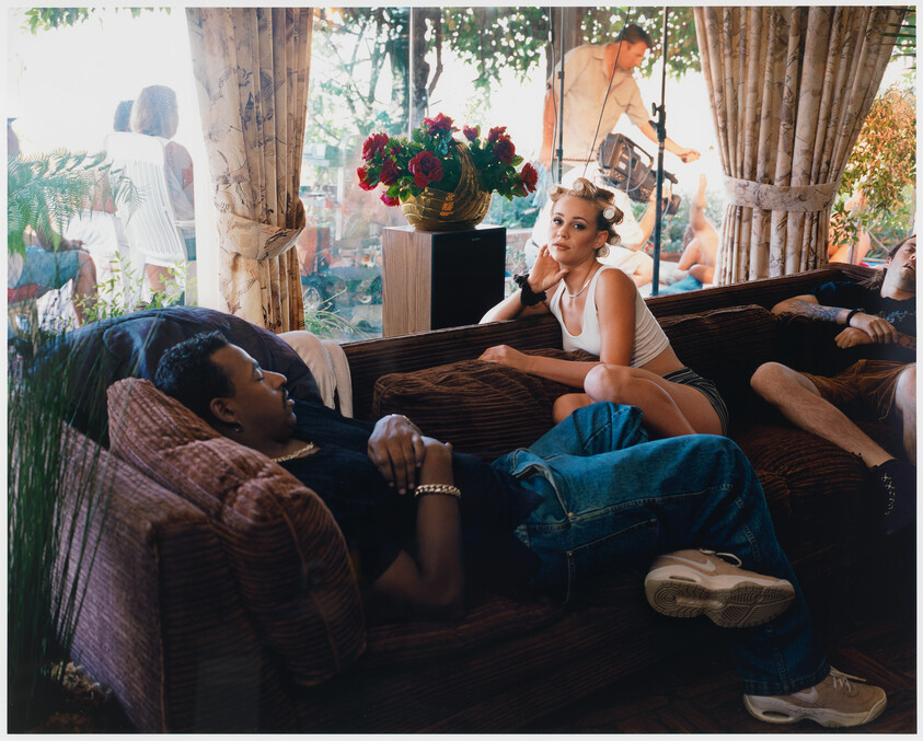 A young woman with hair rollers lounges on a couch while friends relax nearby.