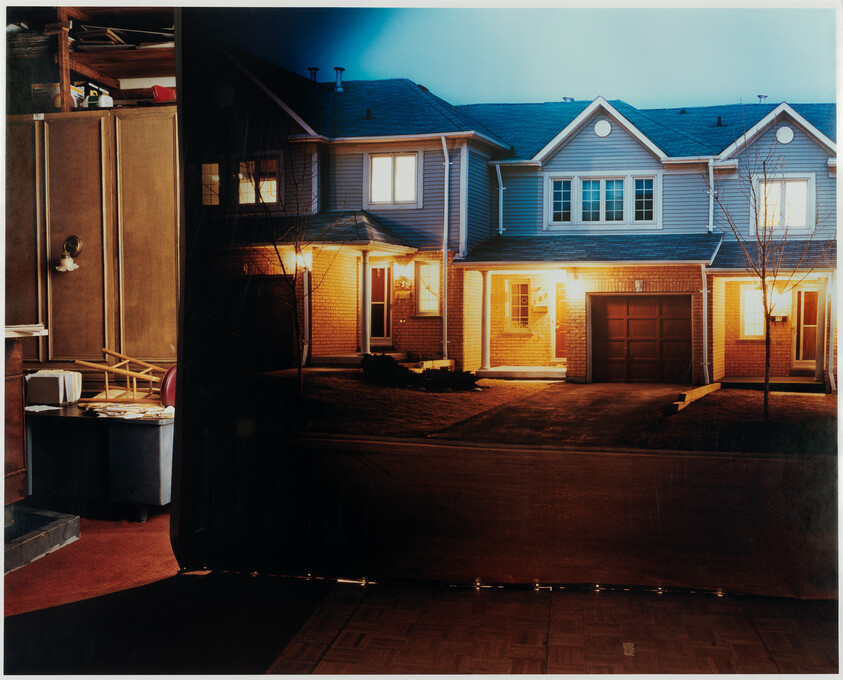 A suburban townhouse with its front lights on and a closed garage at dusk.