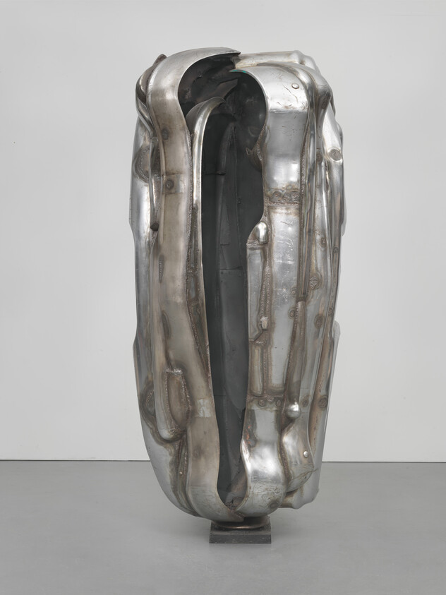 Tall polished metal sculpture with dented, folded surface and a deep vertical opening.