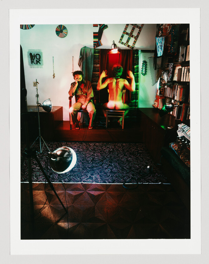 A studio scene shows a seated man smoking while a nude person on stage faces away and raises their arms.