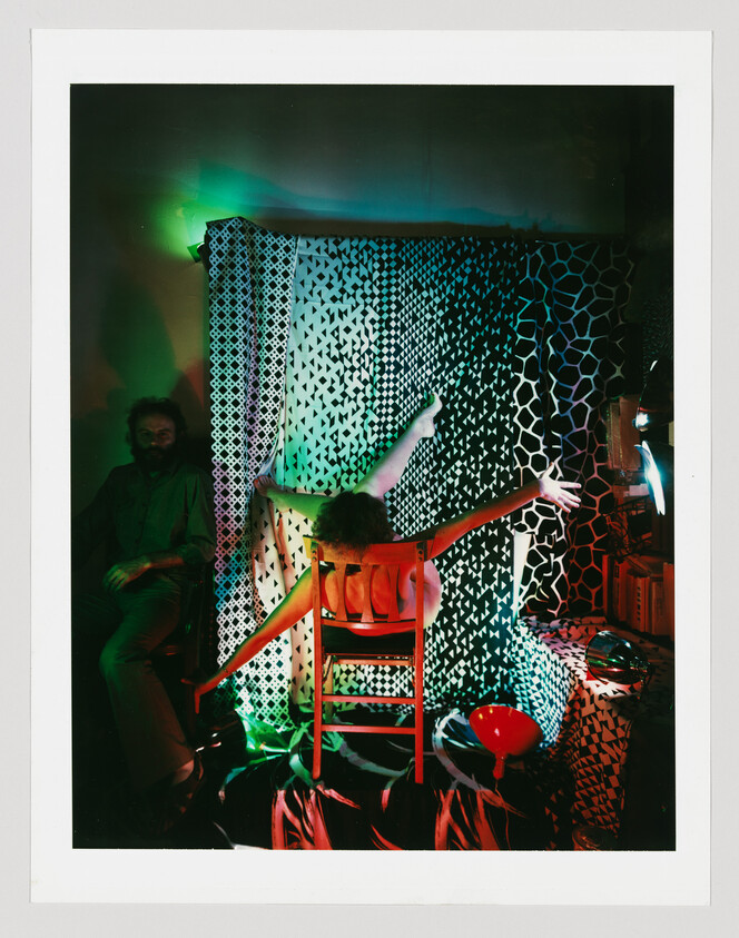 Person sitting backward on a chair with arms outstretched in a colorful, patterned room.