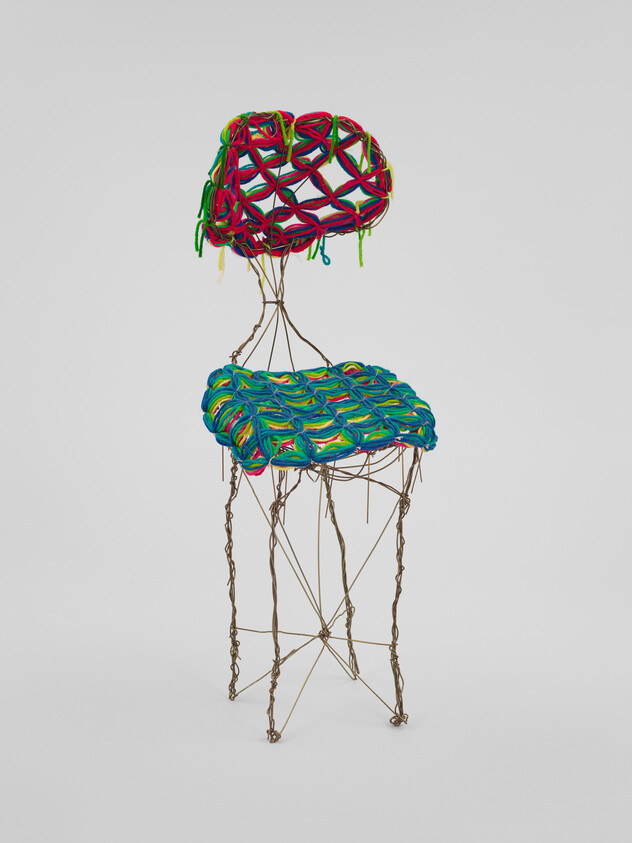 A tall wire-framed chair with bright multicolored woven yarn seat and back.