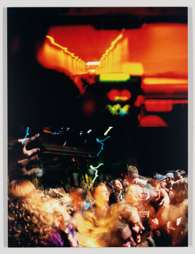 Crowded nightclub dance floor with people dancing under blurred colorful lights and moving beams.