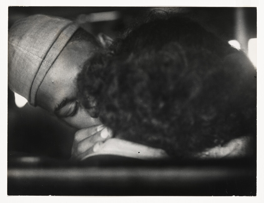 A sailor in uniform kisses a person with curly hair in a close embrace.