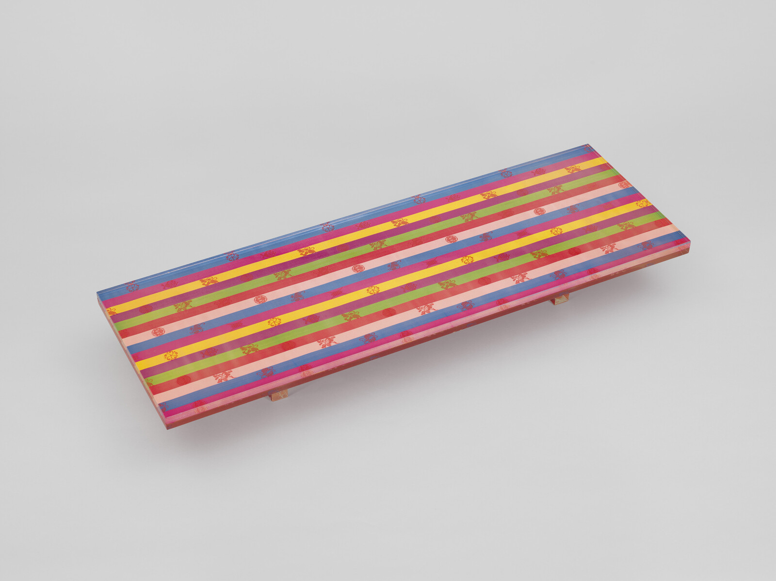 Long wooden bench with bright multicolored horizontal stripes and small floral motifs.