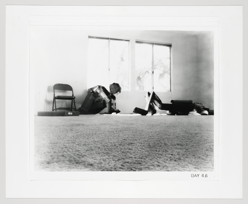 A mostly empty room with a folding chair and scattered boxes and bags near bright windows.
