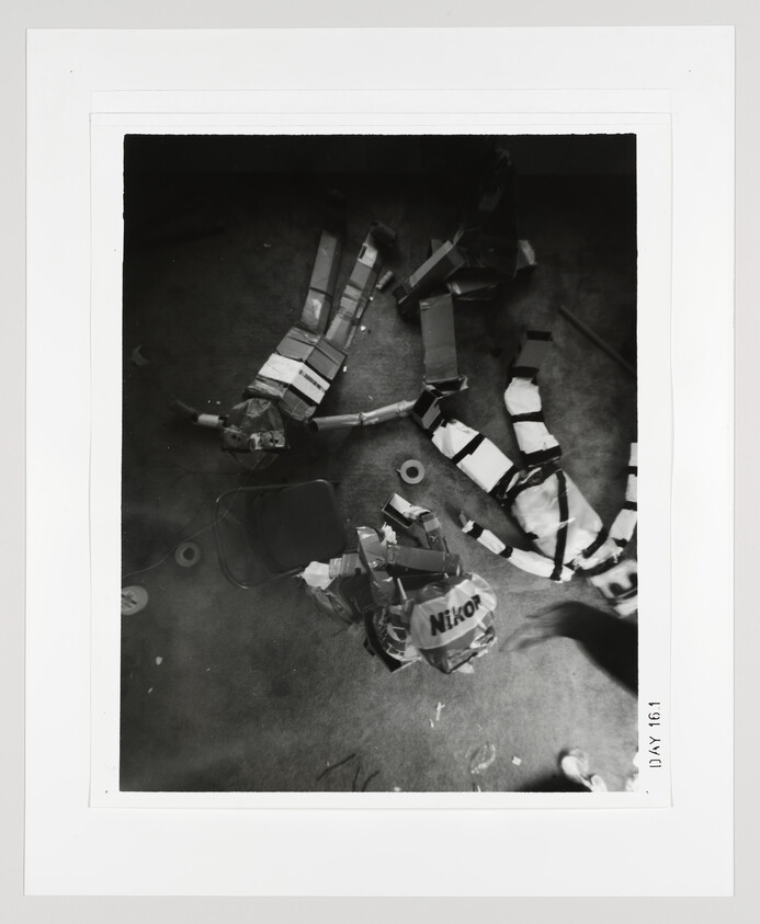 Two homemade cardboard and tape mannequins lie on a floor surrounded by tape rolls and debris.