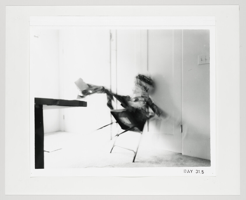 A blurred person falling backward from a chair toward a table in a bright room.