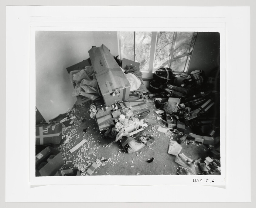 A messy room strewn with open cardboard boxes, packing material, and scattered belongings.