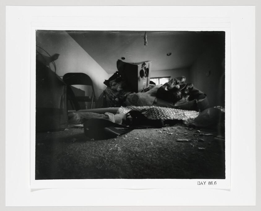 A low-angle view of a cluttered attic room with boxes, bubble wrap, and scattered belongings.