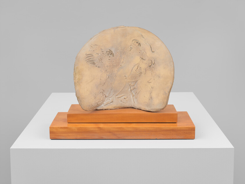 A carved circular stone relief with faint human figures displayed on a two-tier wooden stand.