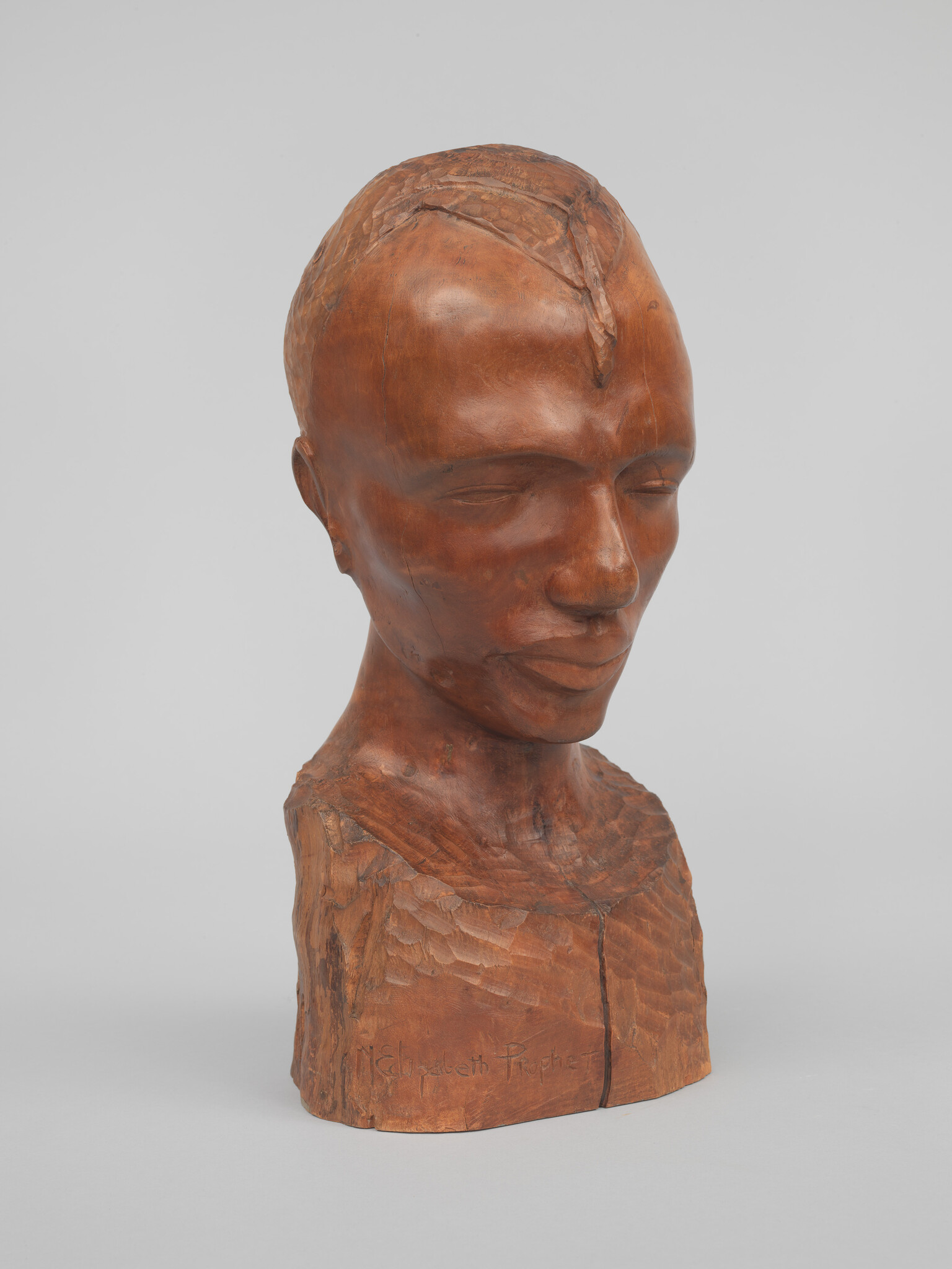 A cherry wood bust of a male head with closed eyes and upturned lips.