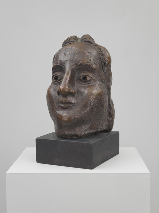 Bronze sculpted head with stylized facial features displayed on a square black plinth.