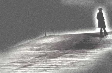 A grainy black and white photo depicting a solitary figure standing on a dimly lit path at night, with a faint light source illuminating the scene from behind. The figure appears to be looking into the distance, and the surrounding area is shrouded in darkness, creating a mysterious and moody atmosphere.