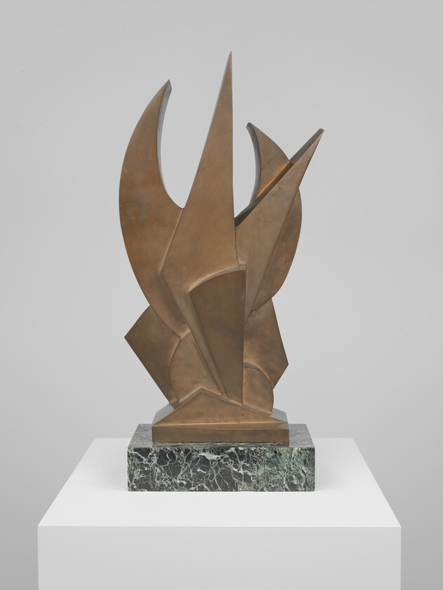 Abstract bronze sculpture with sharp geometric planes stands on a green marble base on a white pedestal.